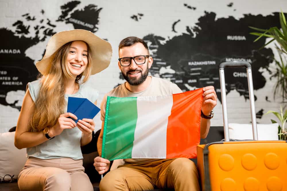 young couple sitting with italian flag passports travel agency office world map background prepairing trip italy min - working holiday visa for Italian Citizens in Immigration Law