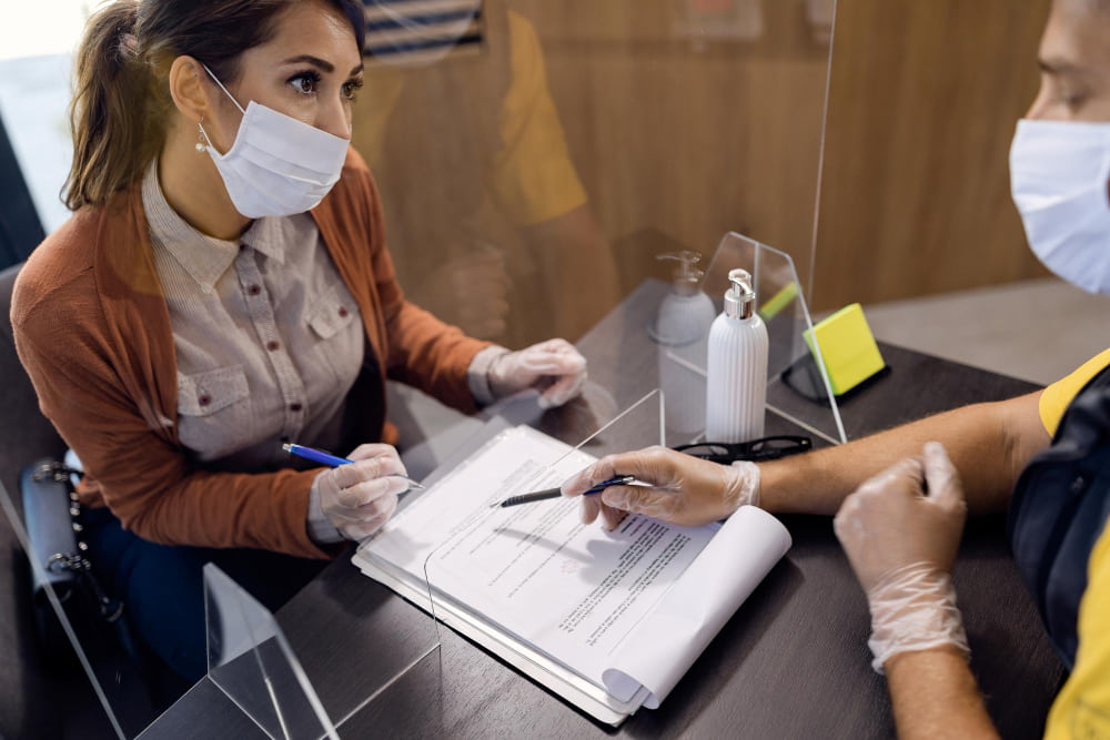 young woman with protective face masks signing documents while talking auto mechanic office min - Force majeure clause in contracts in Commercial and Business Law